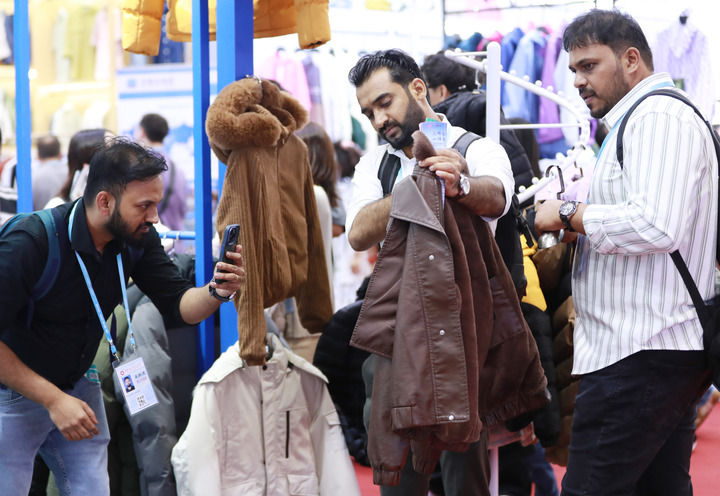 2025年5月1日,在广州开幕的第137届广交会第三期上,境外采购商在一家服装企业的展区拍摄样品。新华社记者 王瑞平 摄.jpg